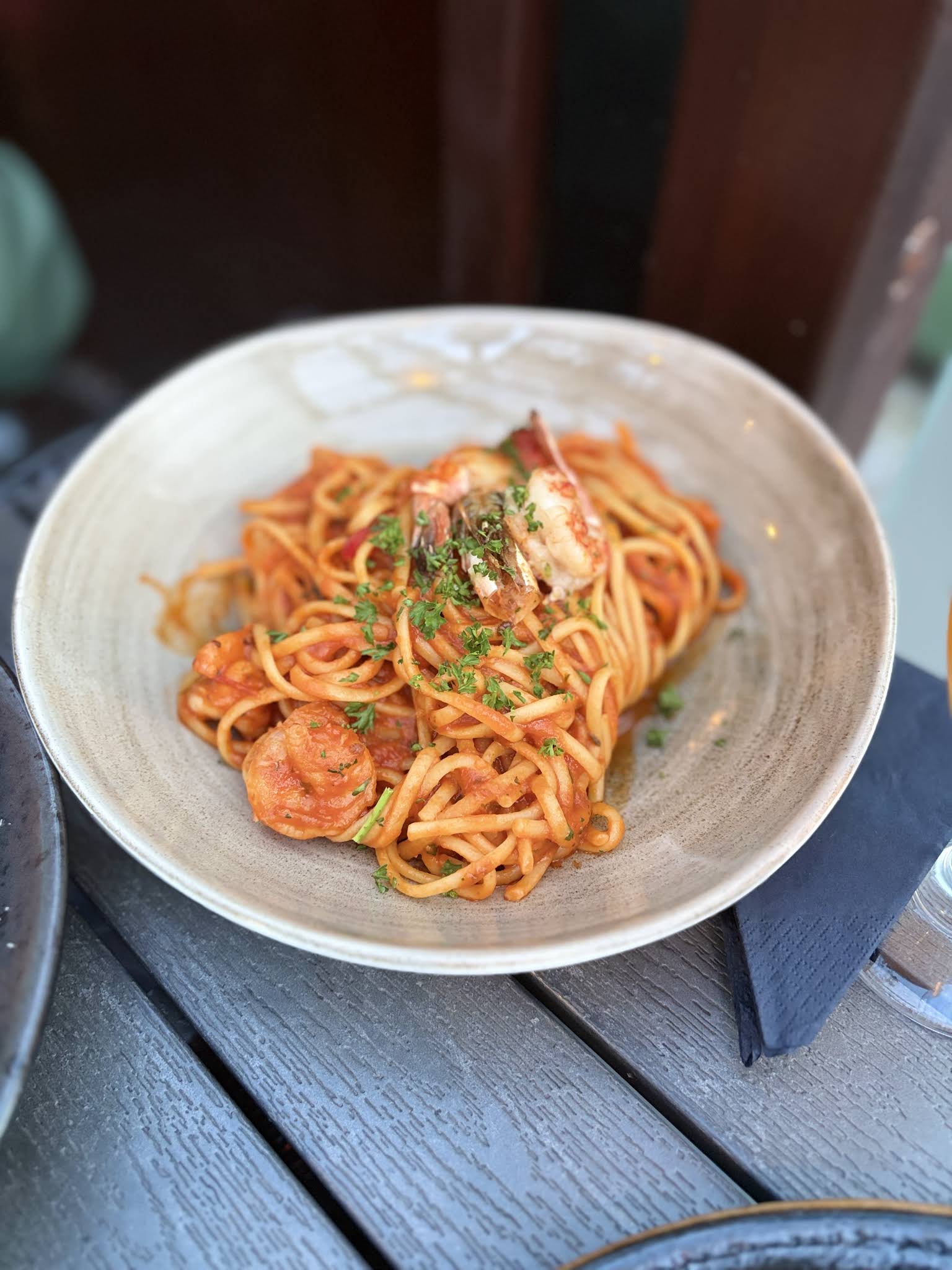 A complete bowl of tomato and prawn linguine at San Pietro Restaurant, on a dark outdoor table